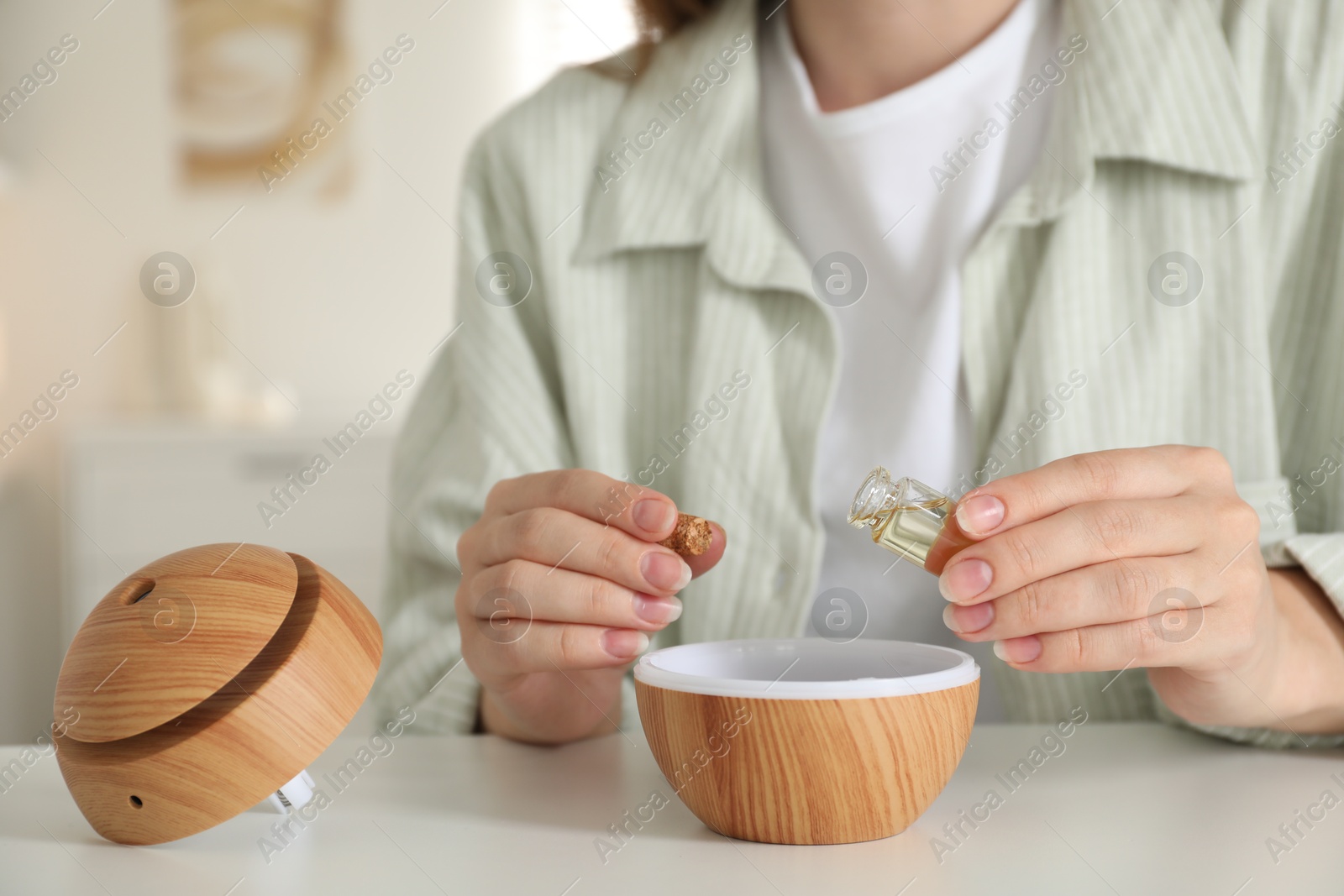 Photo of Woman adding essential oil to aroma diffuser at home, closeup