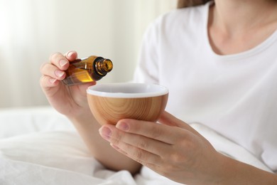 Photo of Woman adding essential oil to aroma diffuser at home, closeup