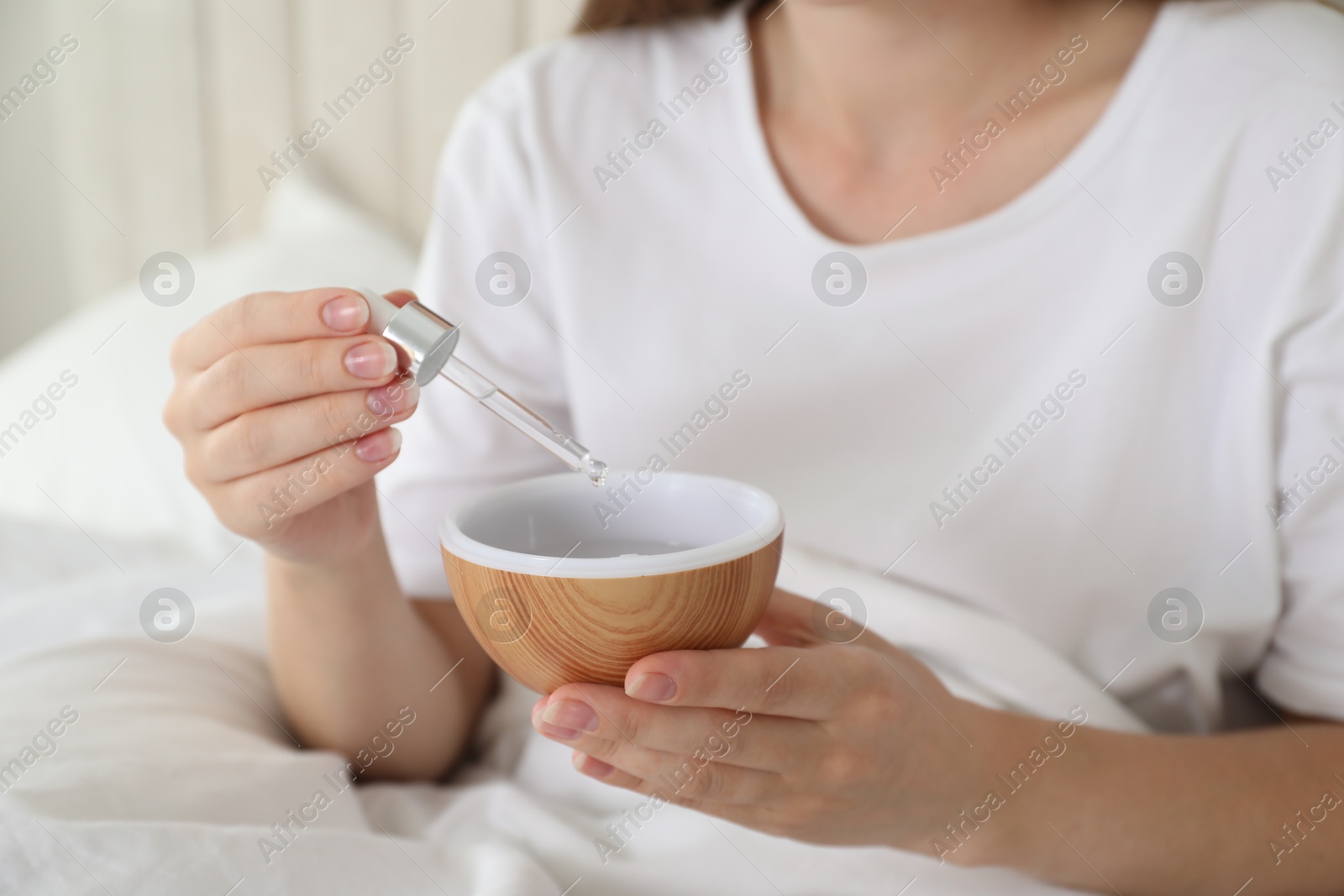 Photo of Woman adding essential oil to aroma diffuser at home, closeup