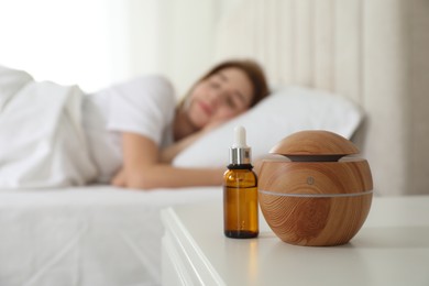 Photo of Woman sleeping at home, focus on aroma diffuser and essential oil