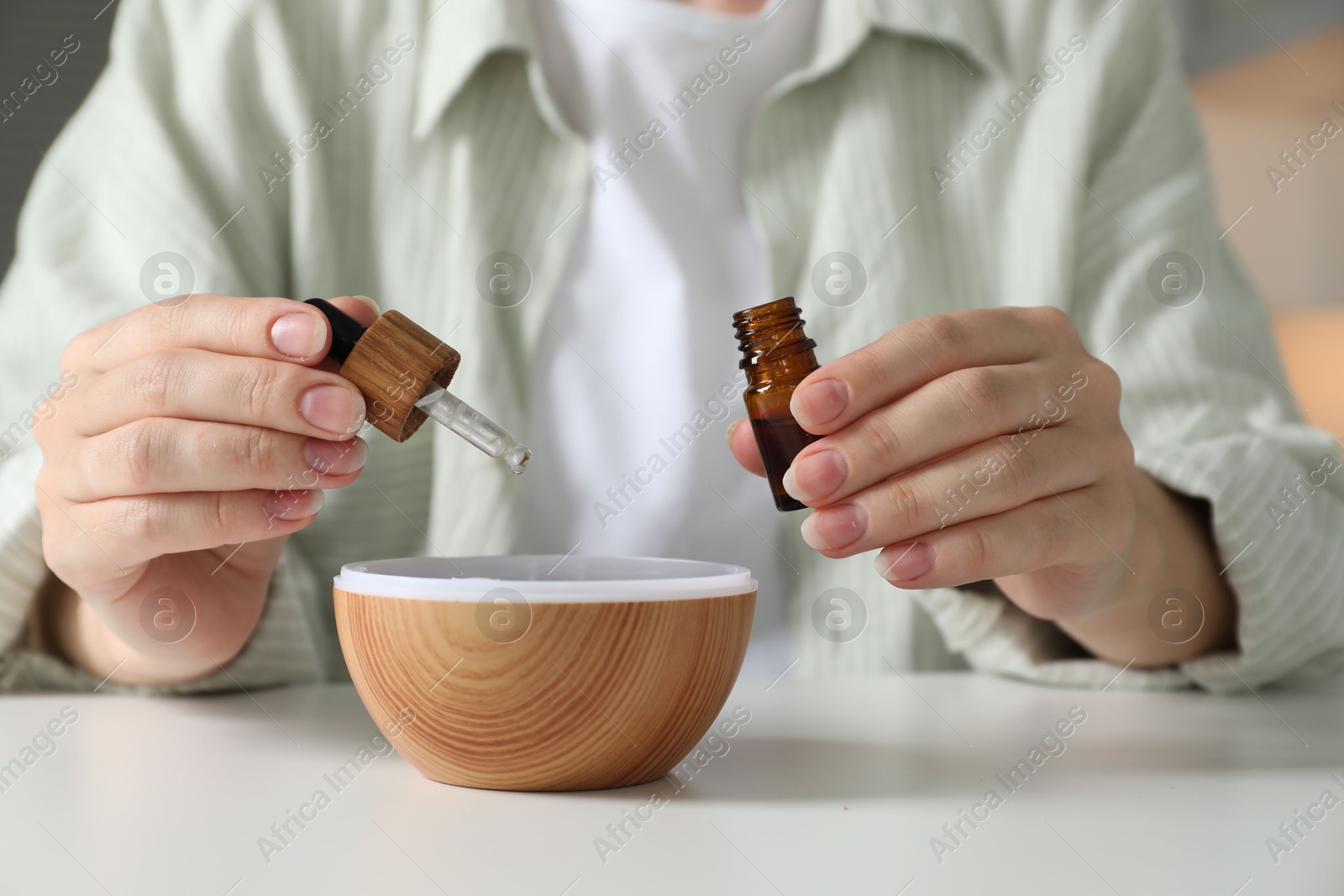 Photo of Woman adding essential oil to aroma diffuser at home, closeup