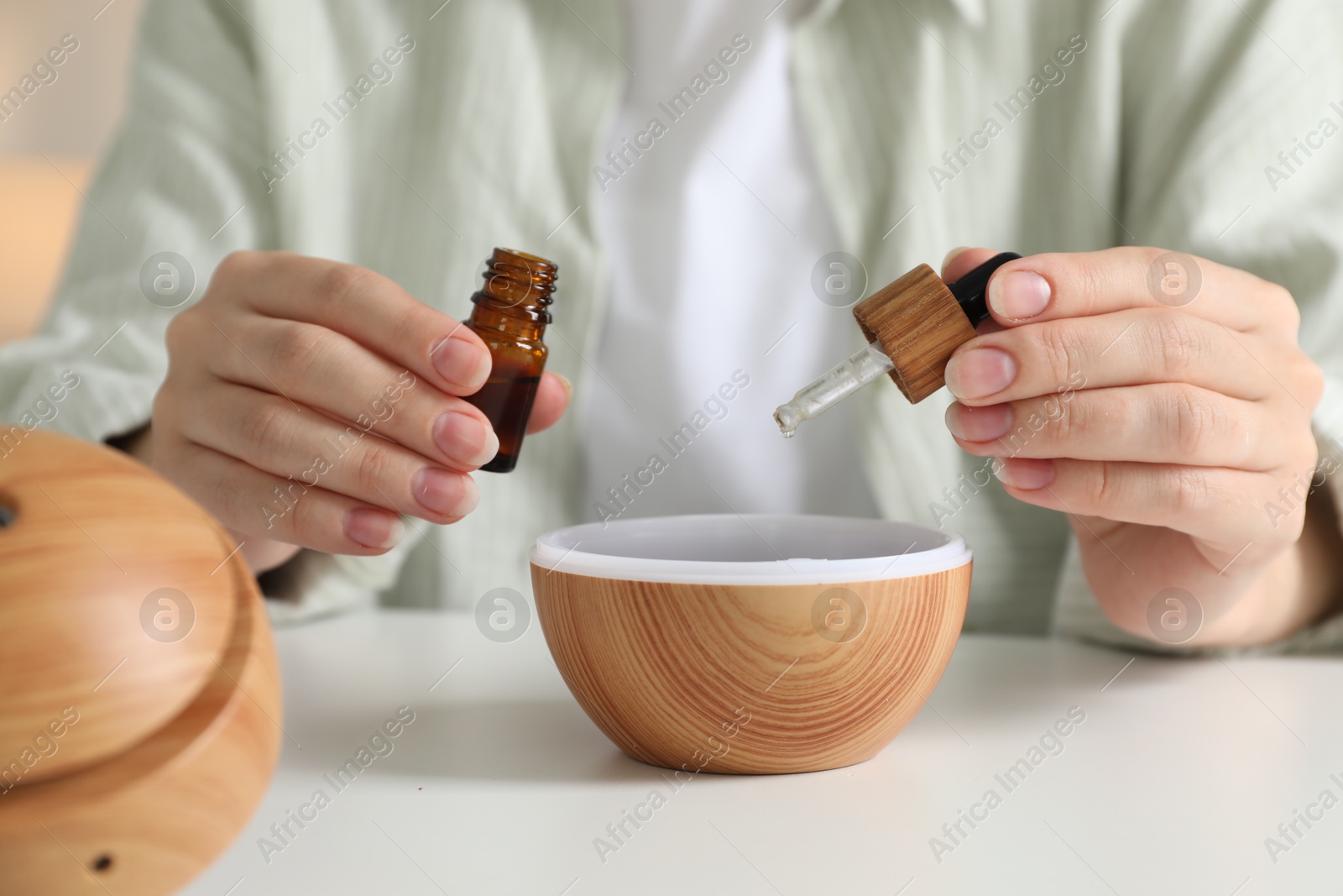 Photo of Woman adding essential oil to aroma diffuser at home, closeup