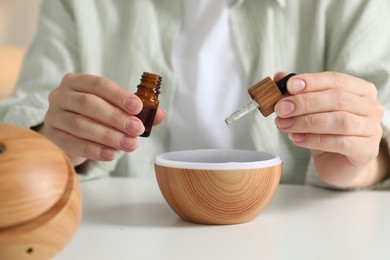 Woman adding essential oil to aroma diffuser at home, closeup