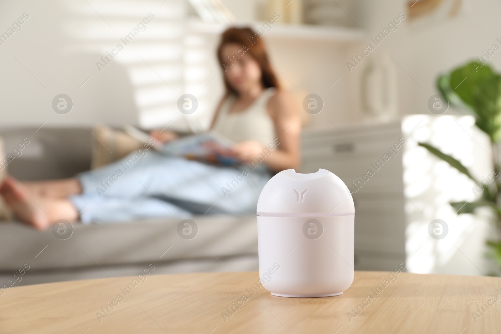 Photo of Woman reading magazine at home, focus on essential oil aroma diffuser