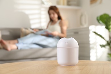 Woman reading magazine at home, focus on essential oil aroma diffuser