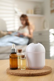 Woman reading magazine at home, focus on bottles of essential oils and aroma diffuser