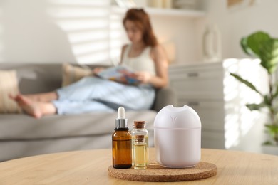 Woman reading magazine at home, focus on bottles of essential oils and aroma diffuser