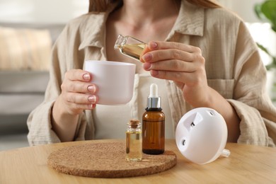 Woman adding essential oil to aroma diffuser at home, closeup