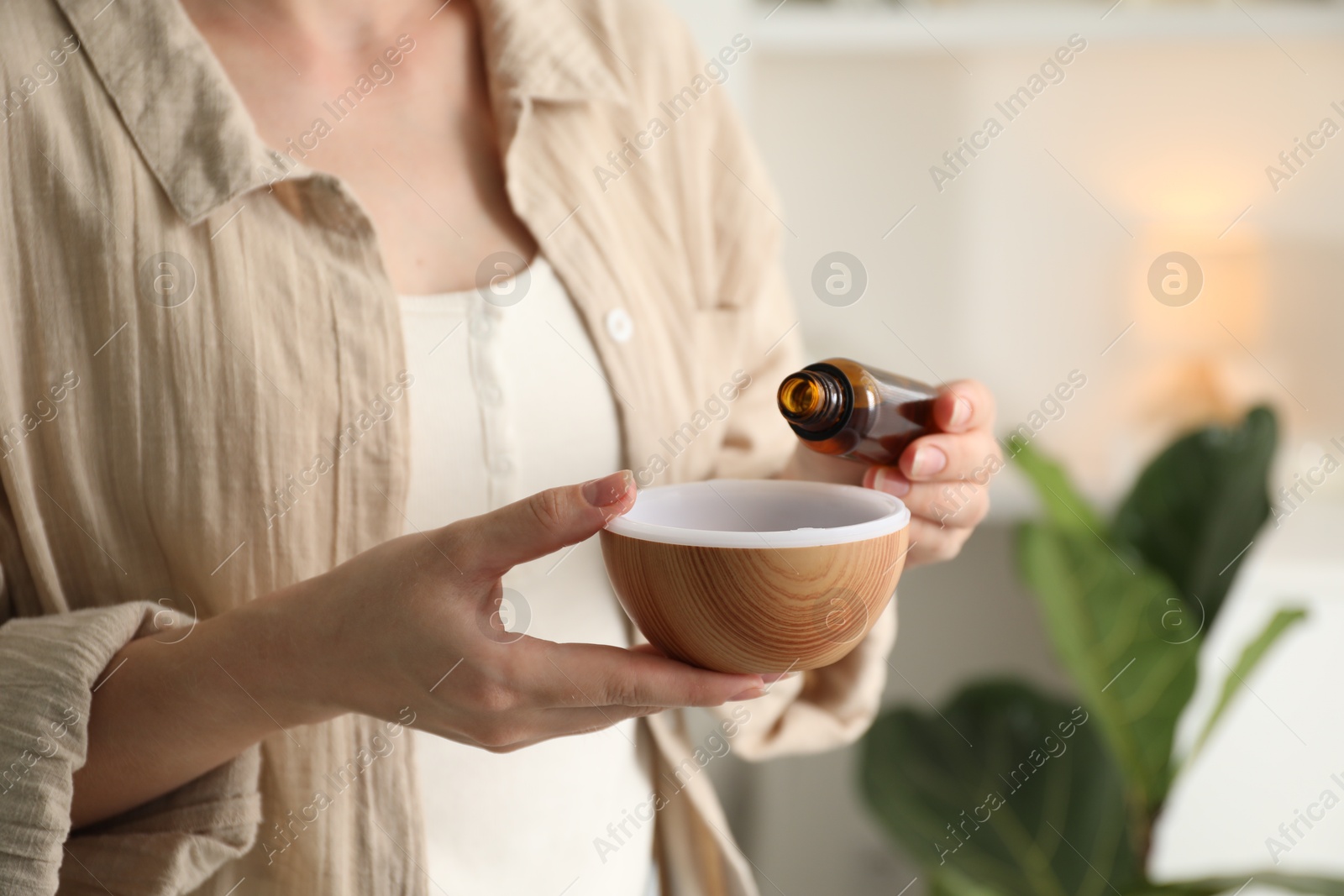 Photo of Woman adding essential oil to aroma diffuser at home, closeup