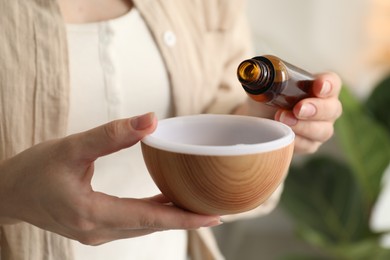 Photo of Woman adding essential oil to aroma diffuser at home, closeup