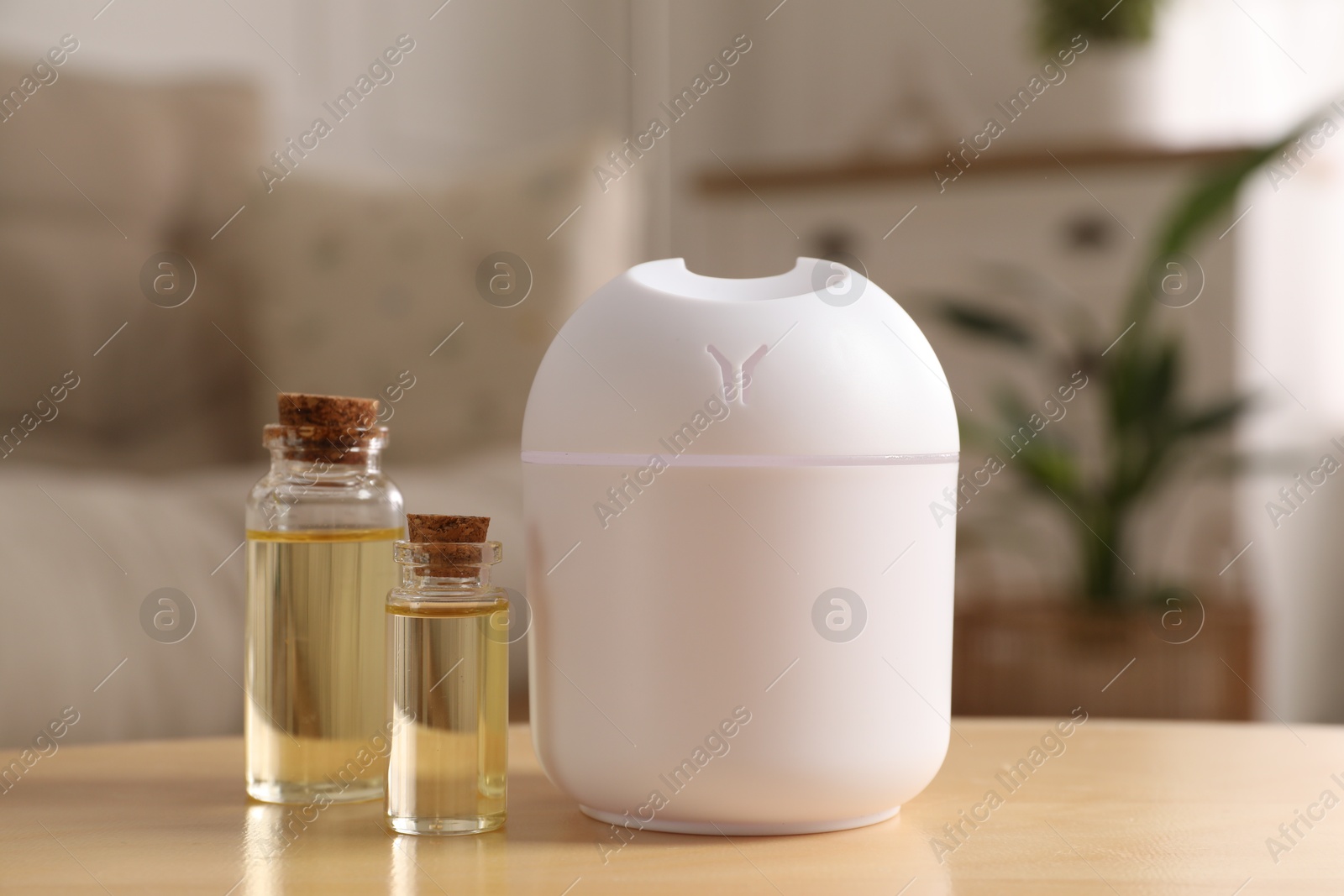 Photo of Aroma diffuser and bottles of essential oils on wooden table at home