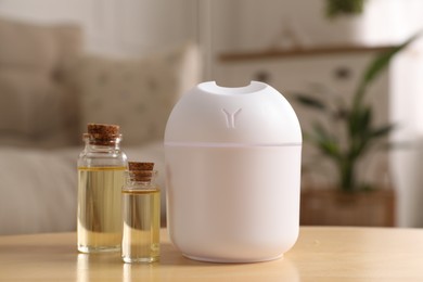 Photo of Aroma diffuser and bottles of essential oils on wooden table at home