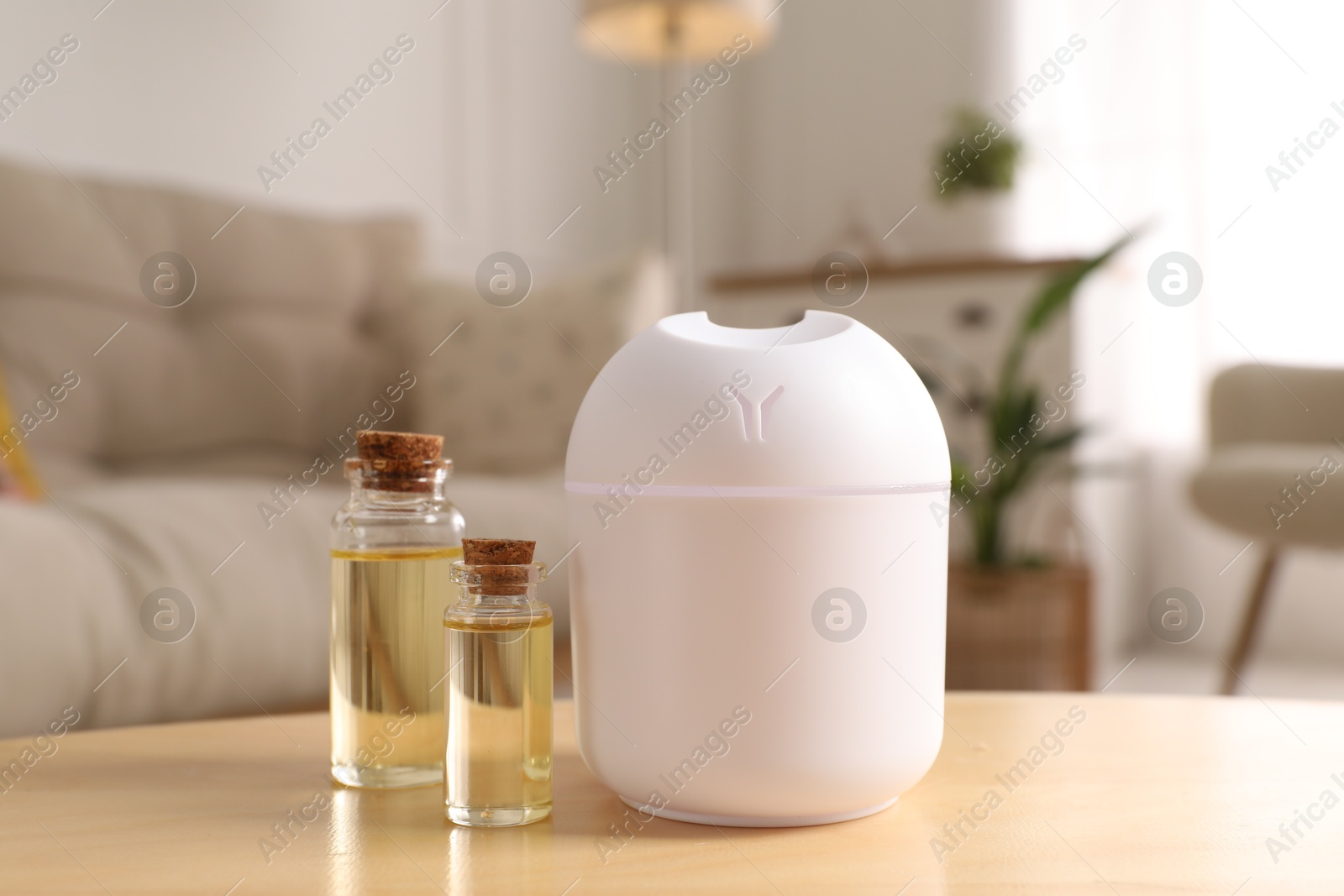 Photo of Aroma diffuser and bottles of essential oils on wooden table at home