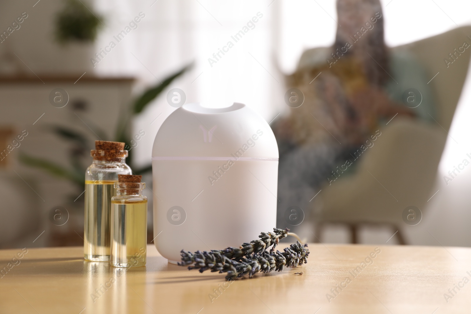 Photo of Woman reading magazine at home, focus on aroma diffuser, bottles of essential oils and lavender flowers