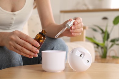 Woman adding essential oil to aroma diffuser at home, closeup