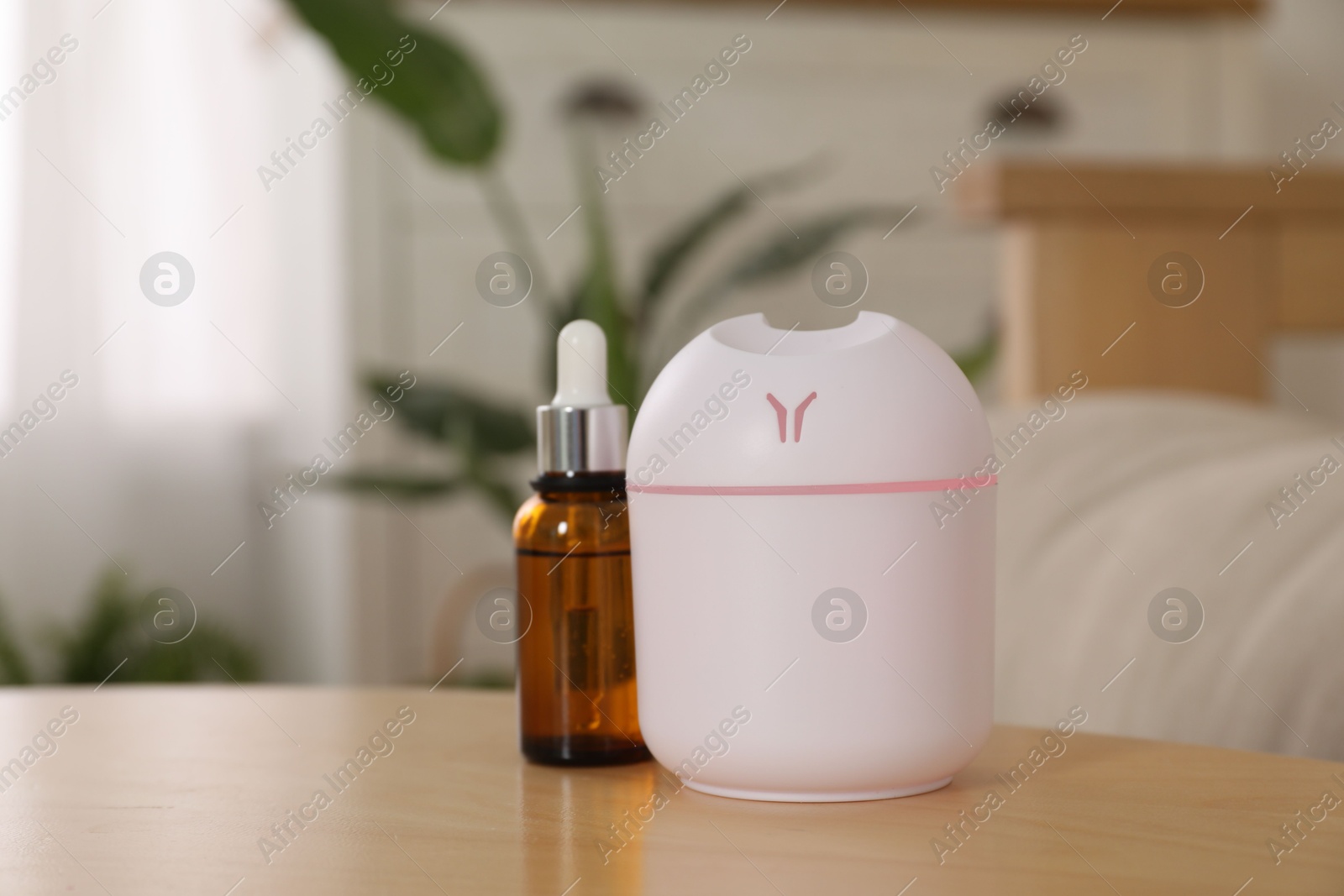 Photo of Aroma diffuser and bottle of essential oil on wooden table at home