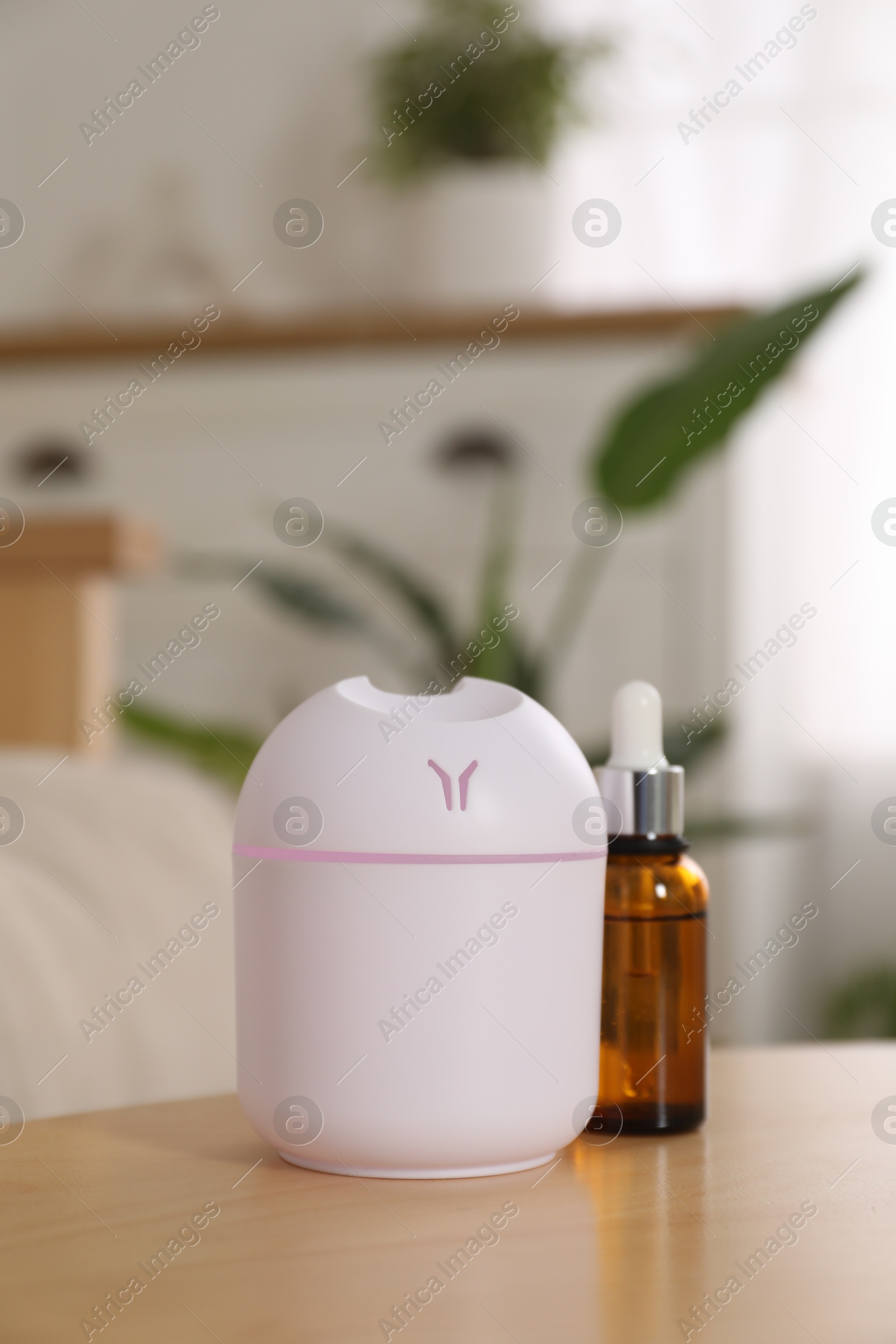 Photo of Aroma diffuser and bottle of essential oil on wooden table at home