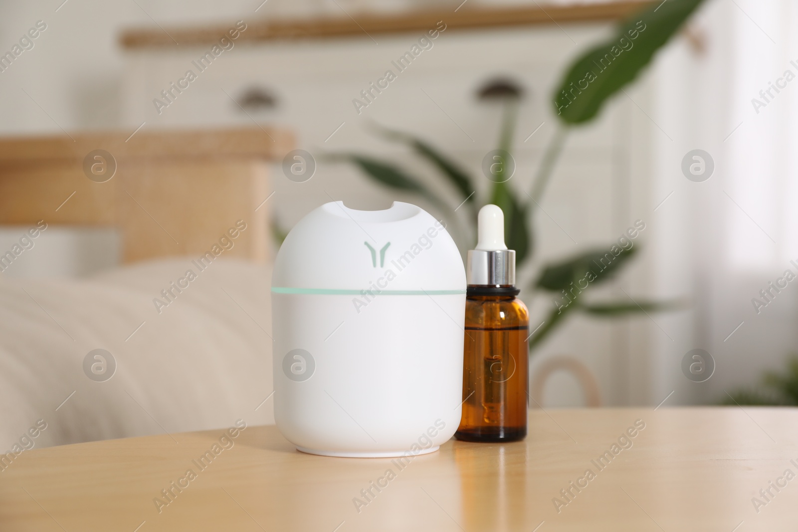 Photo of Aroma diffuser and bottle of essential oil on wooden table at home