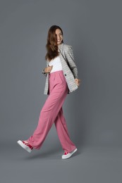 Photo of Beautiful woman in stylish jacket and pink pants on grey background