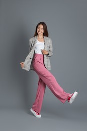 Photo of Beautiful woman in stylish jacket and pink pants on grey background