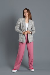 Beautiful woman in stylish jacket and pink pants on grey background