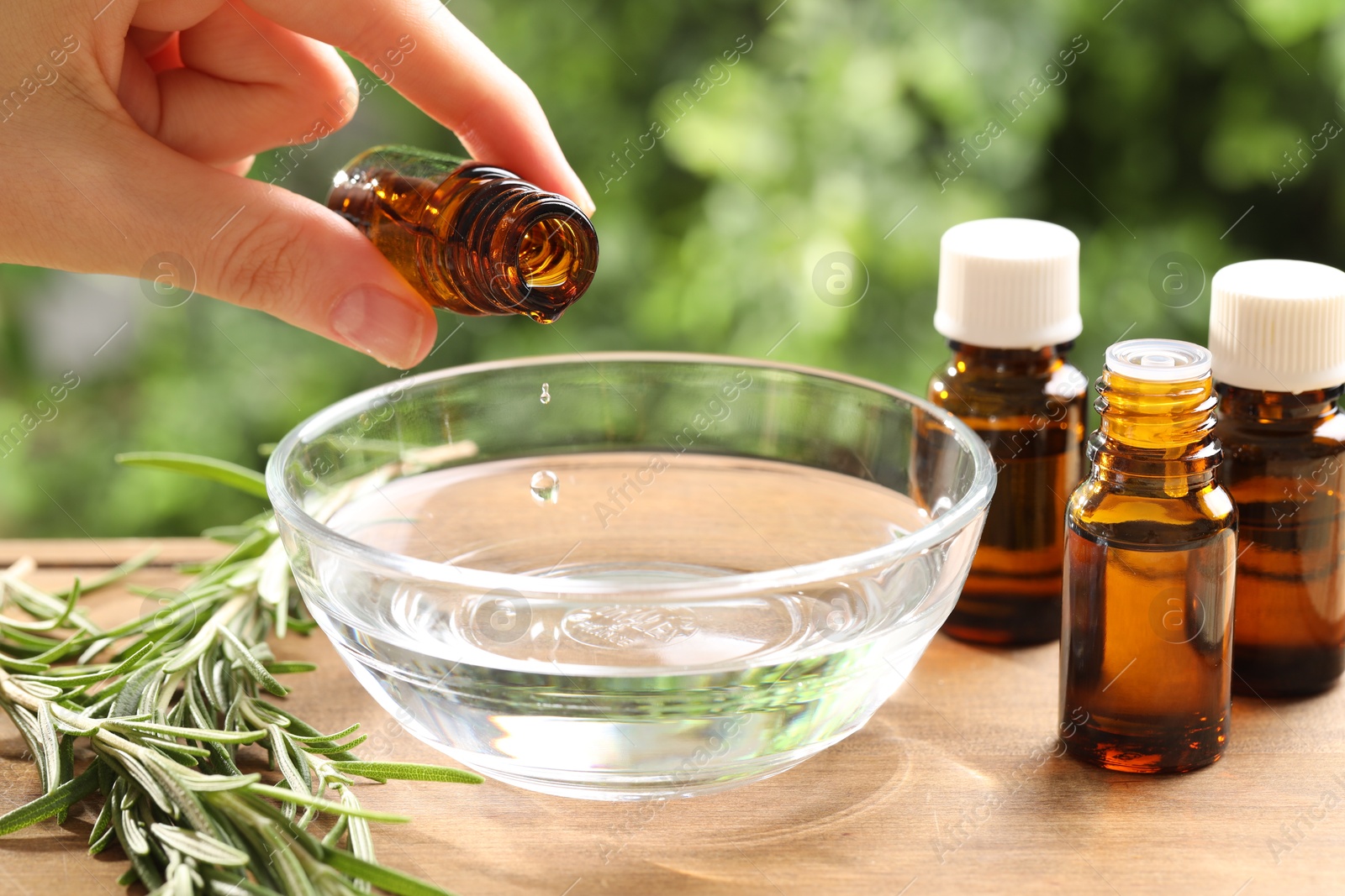 Photo of Woman dripping essential oil into bowl at wooden table, closeup