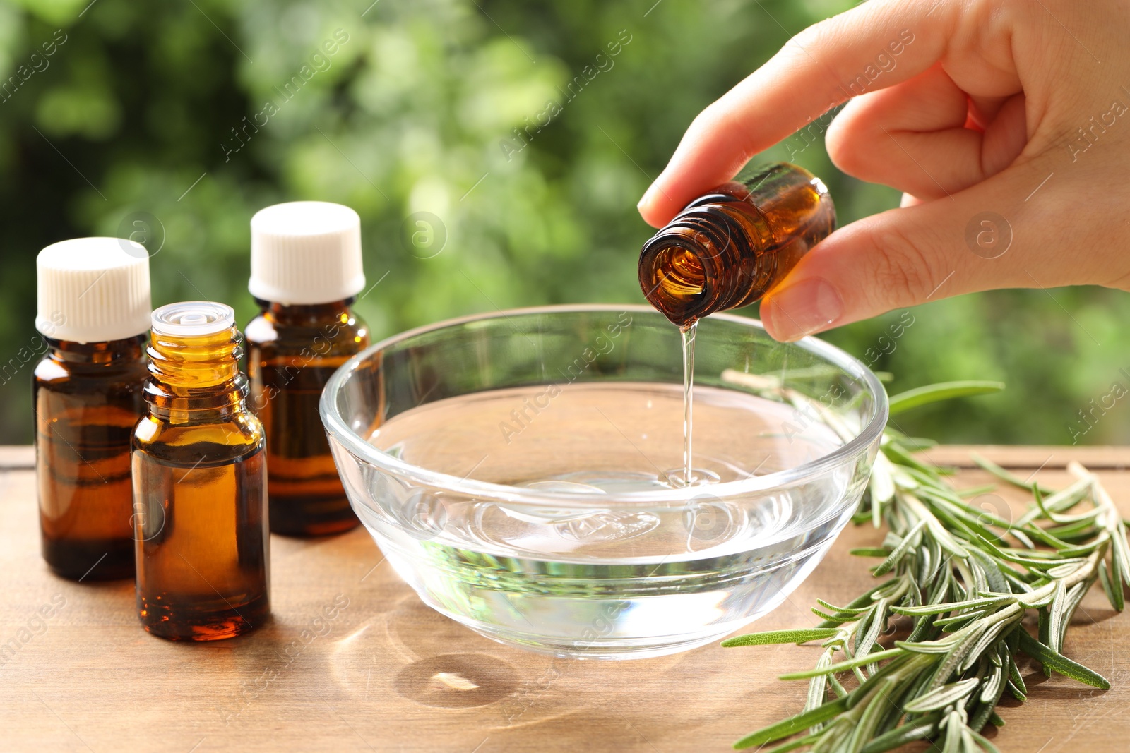 Photo of Woman dripping essential oil into bowl at wooden table, closeup