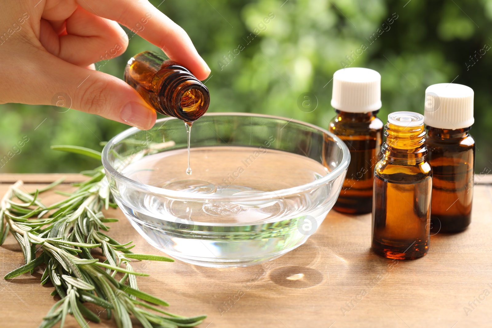 Photo of Woman dripping essential oil into bowl at wooden table, closeup