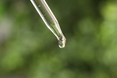 Photo of Essential oil dripping from pipette on blurred background, closeup