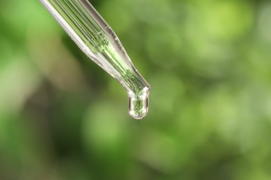 Photo of Essential oil dripping from pipette on blurred background, closeup