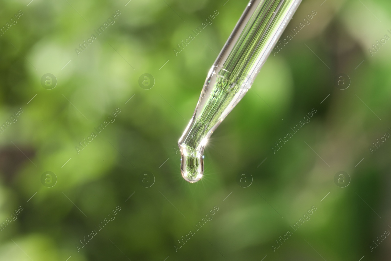 Photo of Essential oil dripping from pipette on blurred background, closeup