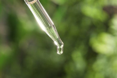 Photo of Essential oil dripping from pipette on blurred background, closeup