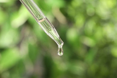 Photo of Essential oil dripping from pipette on blurred background, closeup