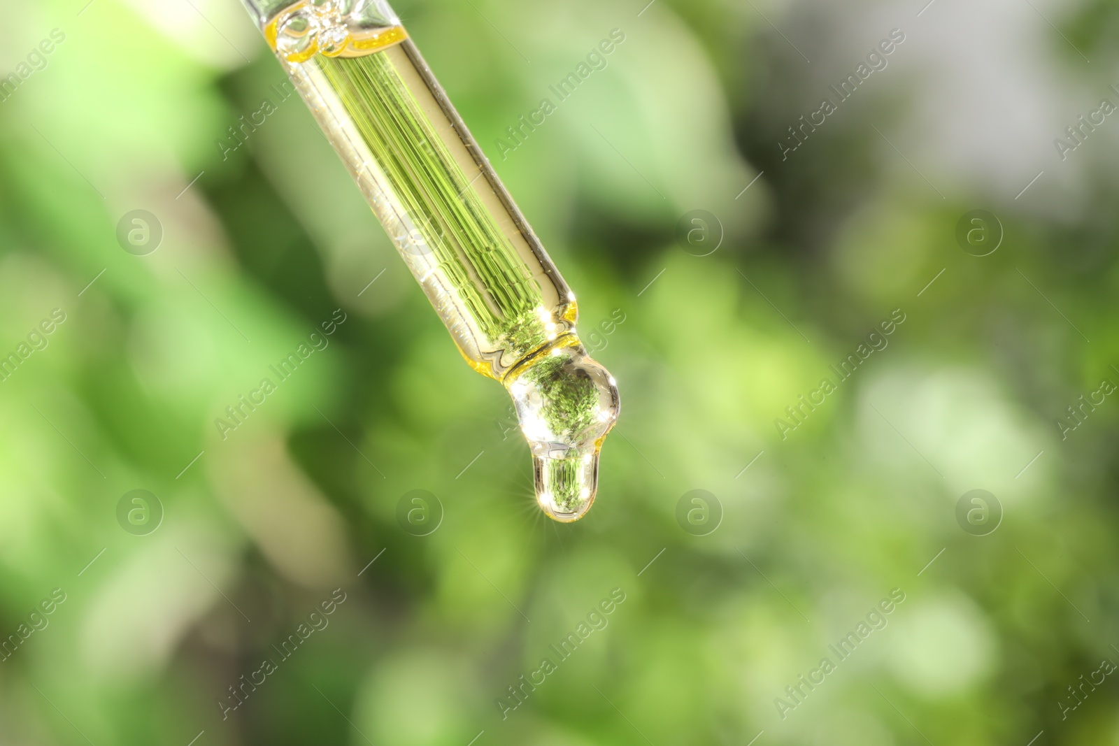 Photo of Essential oil dripping from pipette on blurred background, closeup