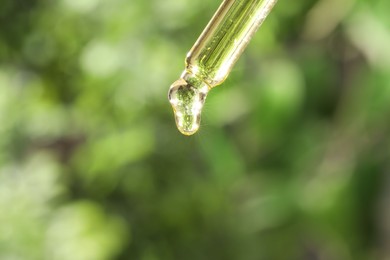 Essential oil dripping from pipette on blurred background, closeup