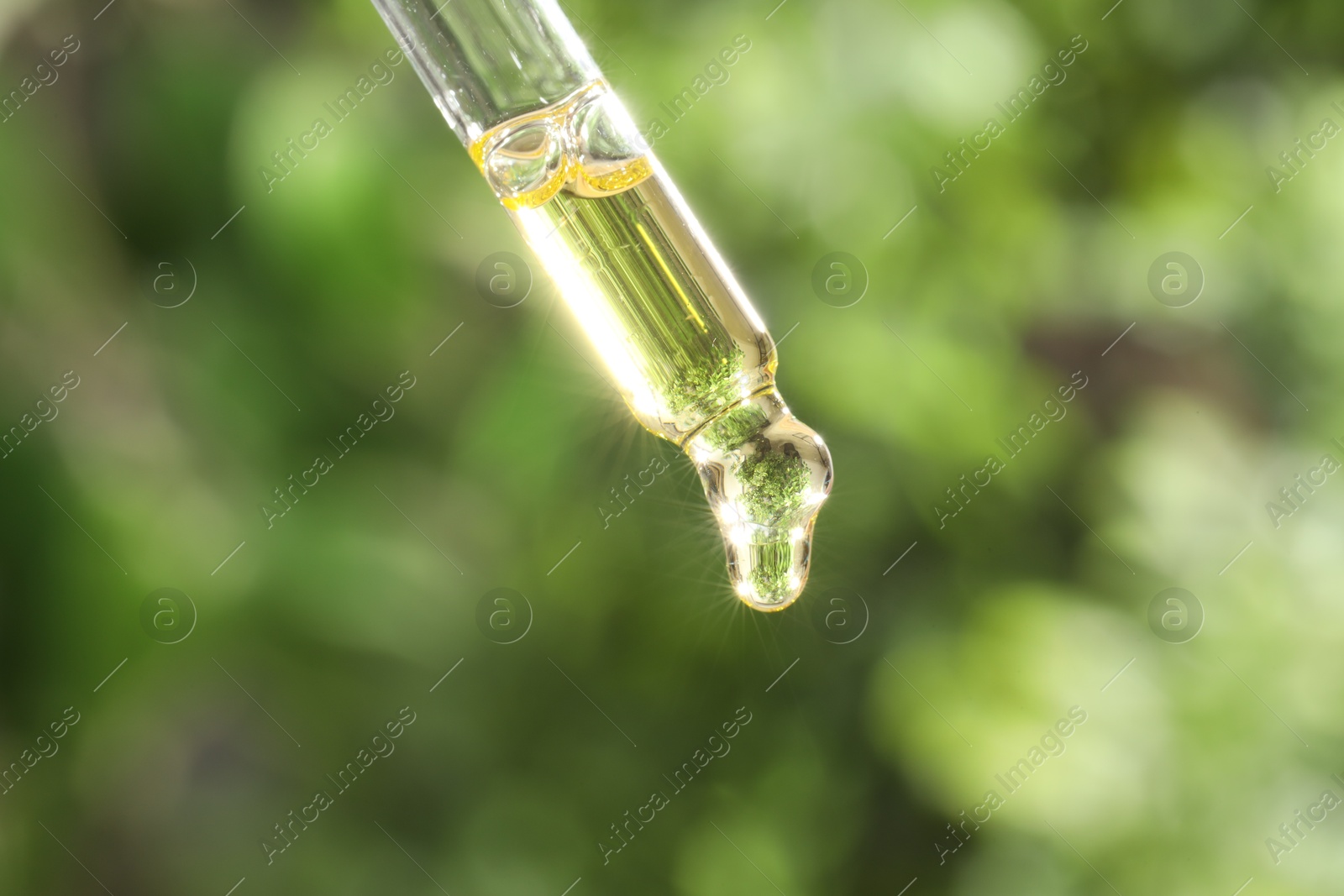 Photo of Essential oil dripping from pipette on blurred background, closeup