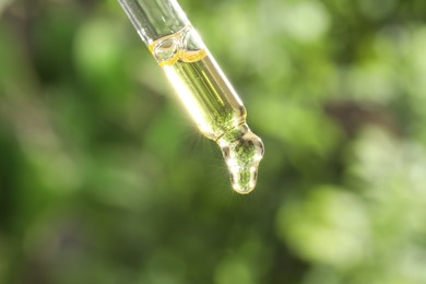 Photo of Essential oil dripping from pipette on blurred background, closeup