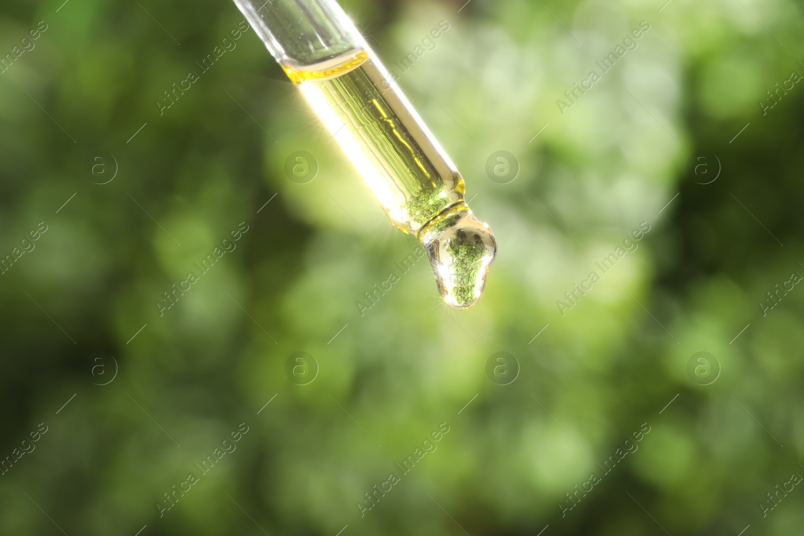 Photo of Essential oil dripping from pipette on blurred background, closeup