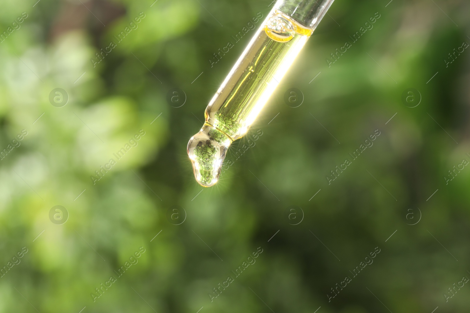 Photo of Essential oil dripping from pipette on blurred background, closeup