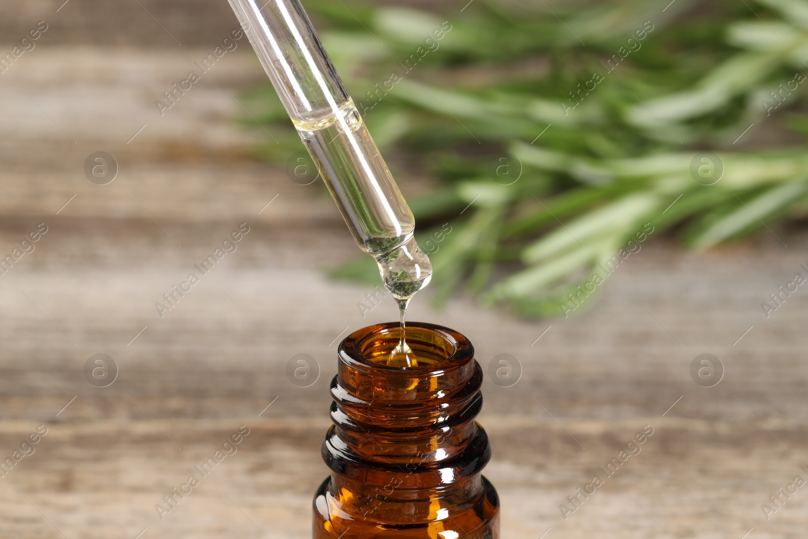 Photo of Dripping essential oil into bottle on wooden table, closeup