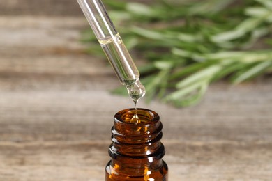 Dripping essential oil into bottle on wooden table, closeup