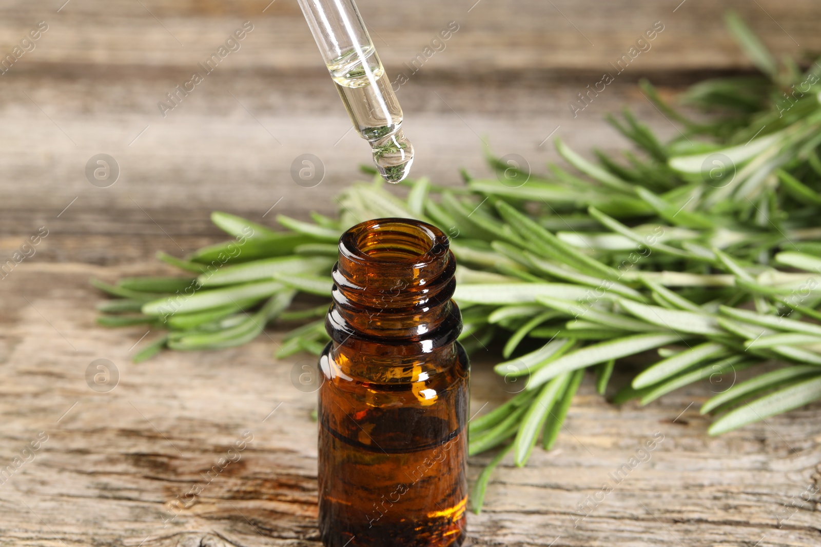 Photo of Dripping essential oil into bottle on wooden table, closeup