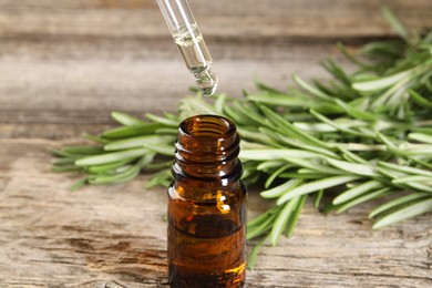 Photo of Dripping essential oil into bottle on wooden table, closeup