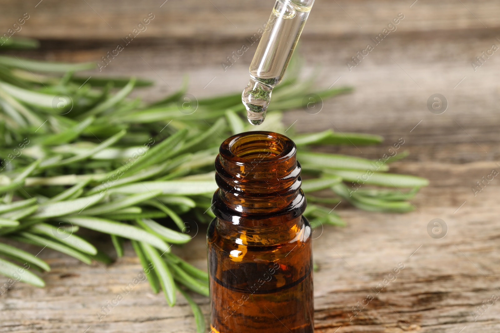 Photo of Dripping essential oil into bottle on wooden table, closeup