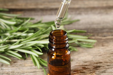 Dripping essential oil into bottle on wooden table, closeup