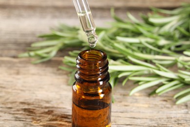 Photo of Dripping essential oil into bottle on wooden table, closeup