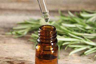 Photo of Dripping essential oil into bottle on wooden table, closeup