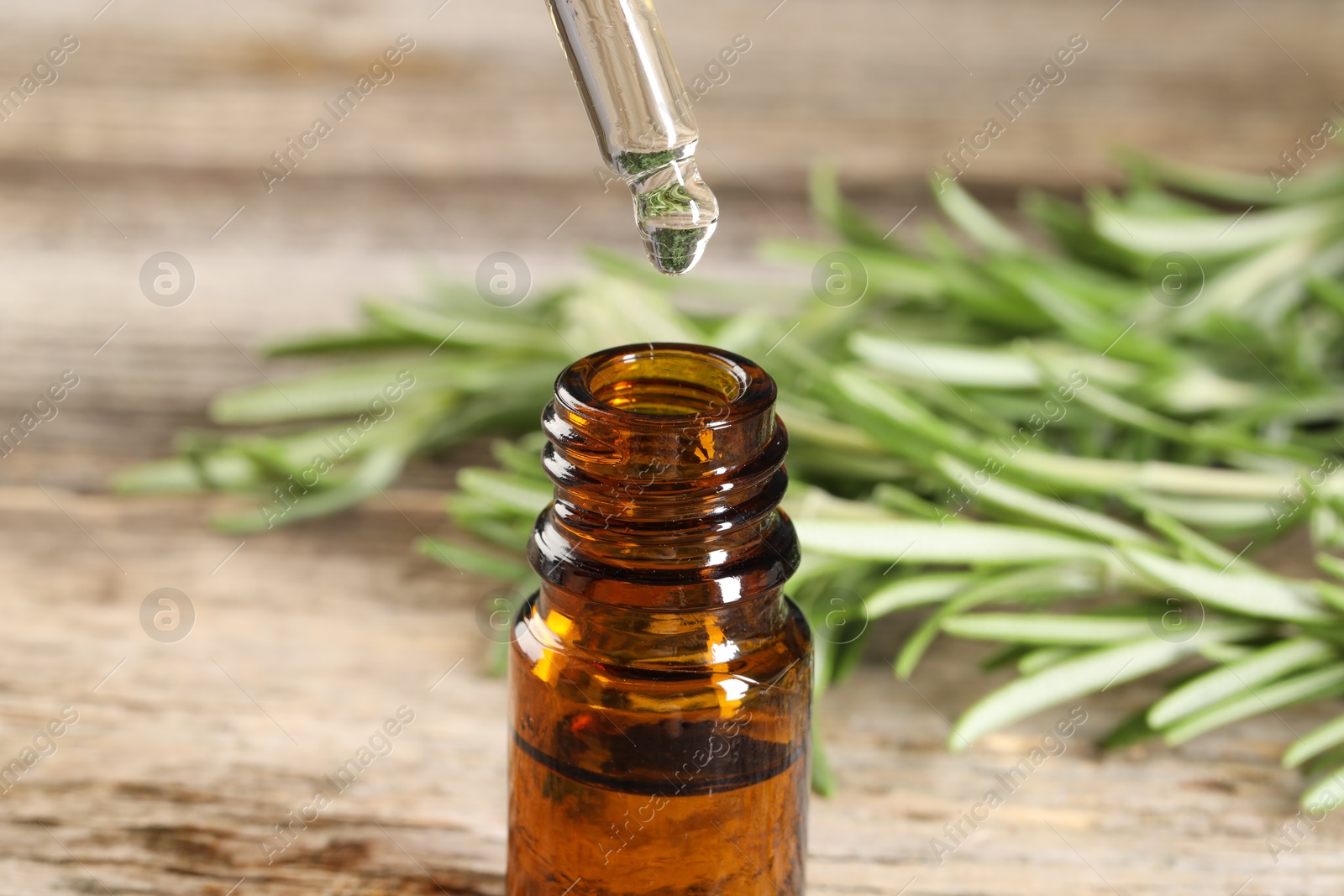 Photo of Dripping essential oil into bottle on wooden table, closeup