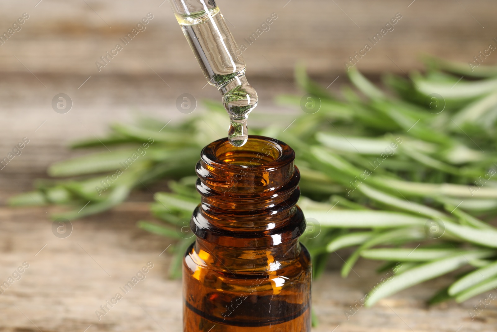 Photo of Dripping essential oil into bottle on wooden table, closeup