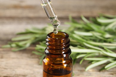 Photo of Dripping essential oil into bottle on wooden table, closeup